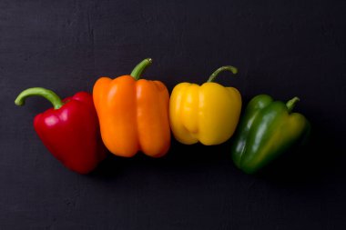 Parlak renkli dolmalık biberler siyah ve modern bir arka planda yatar. Kırmızı biber, turuncu, sarı ve yeşil dolma biber. Düz yat, üst görüş, maket yap. Boşluğu kopyala.