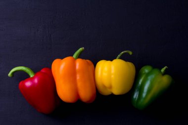 Parlak renkli dolmalık biberler siyah ve modern bir arka planda yatar. Kırmızı biber, turuncu, sarı ve yeşil dolma biber. Düz yat, üst görüş, maket yap. Boşluğu kopyala.