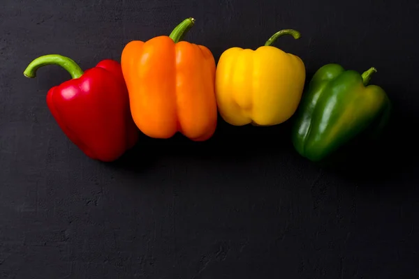 Bright multi-colored bell peppers lie on a black modern concrete background. Red peppers, orange, yellow and green bell peppers. Flat lay, top view, mock up. Copy space.