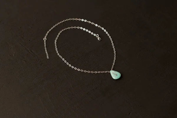 Pendant made of natural turquoise on a silver chain on a black background. Jewelry from natural stones.