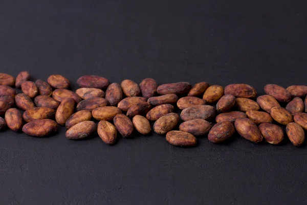 Unpeeled raw brown cocoa beans in heap lie On black modern concrete background. Flat lay, mock up, copy space. Raw materials for making cocoa powder, cocoa beverages, chocolate. Health drink concept.