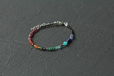 Doğal taşlardan yapılmış parlak bir bilezik. Carnelian, amazonit, turkuaz, siyah dönme, yakut ve zümrüt. El yapımı mücevherler. Siyah modern arka planda el yapımı bilezikler.