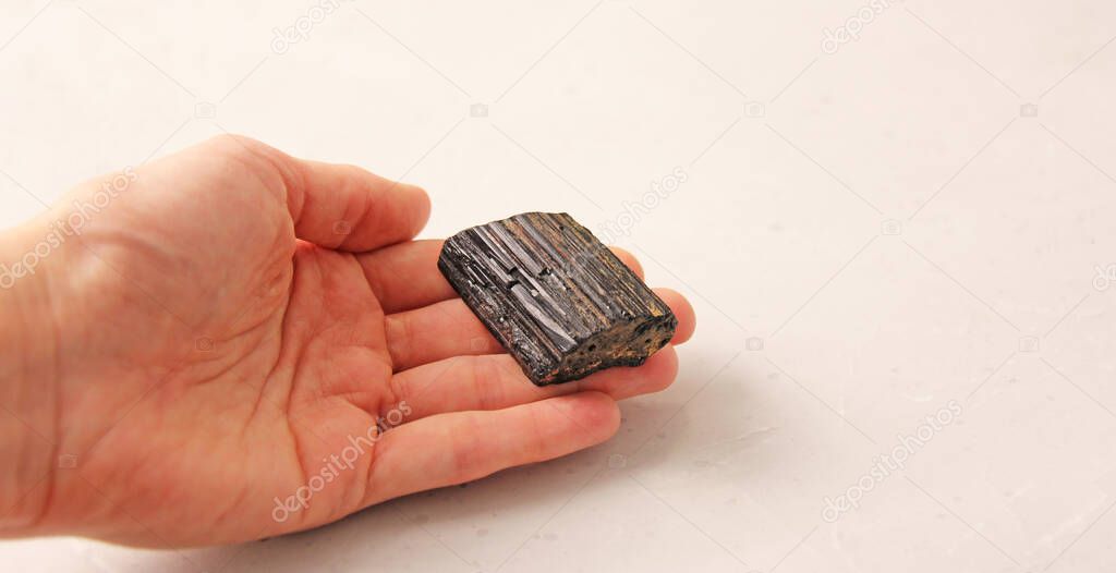 Natural black tourmaline sherl stone is on a woman's hand, in the palm of her hand, on a light background. Natural stones, crystals for magic, lithotherapy, geology, minerals, stone collection.