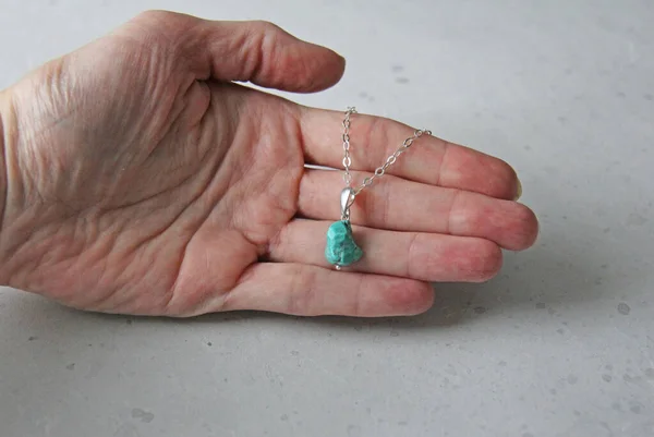 A pendant made of natural stone Turquoise silver chain lies on a woman\'s hand. Author\'s jewelry from natural stones. Designer jewelry. On a light modern background. Natural minerals.