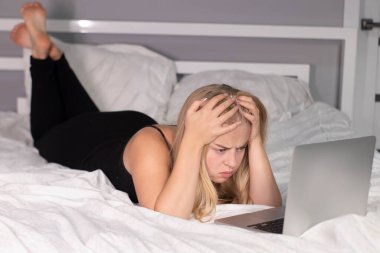 Dizüstü bilgisayarlı, beyaz çarşaflı güzel, bitkin bir sarışın. Tecritteki güzel insanlar