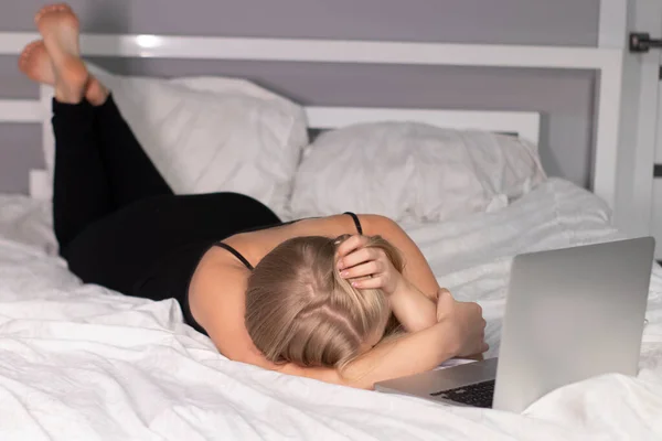 beautiful exhausted blonde with laptop on bed with white sheets. pretty people at isolation
