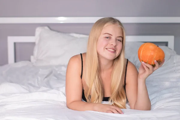 Hermosa rubia feliz con una calabaza en la cama con sábanas blancas. concepto de Halloween — Foto de Stock