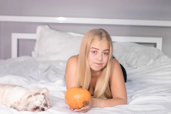 Красивая счастливая блондинка с тыквой на кровати с белыми простынями. Хэллоуин — стоковое фото
