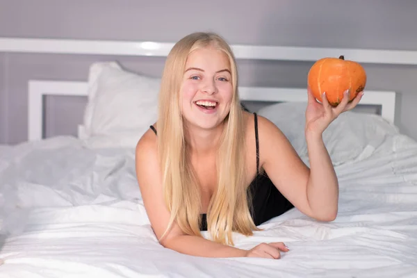 Hermosa rubia feliz con una calabaza en la cama con sábanas blancas. concepto de Halloween — Foto de Stock
