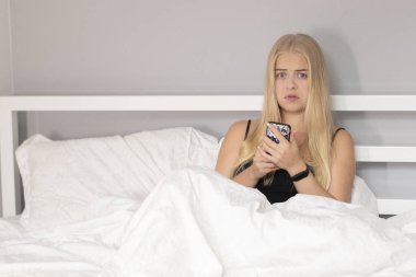 Beyaz yatakta telefonlu düşünceli sarışın. Güzel insanlar tecrit altında