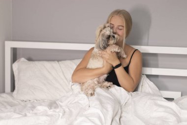 Beyaz çarşaflı köpek yavrusu Shih-tzu ile güzel bir sarışın. Güzel insanlar ve evcil hayvanlar tecrit altında