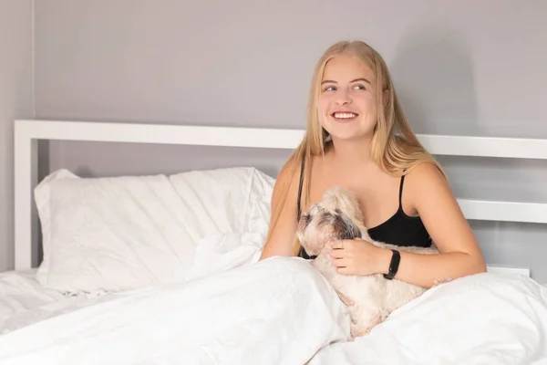 Mooi blond met een puppy shih-tzu op bed met witte lakens. mooie mensen en huisdieren op isolatie — Stockfoto