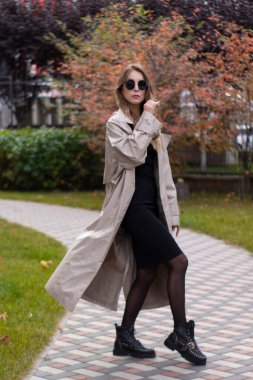 Havalı siperlerde, siyah elbiseli ve parkta güneş gözlüklü çekici, zayıf, genç bir esmer. Sonbahar, sarı yapraklar