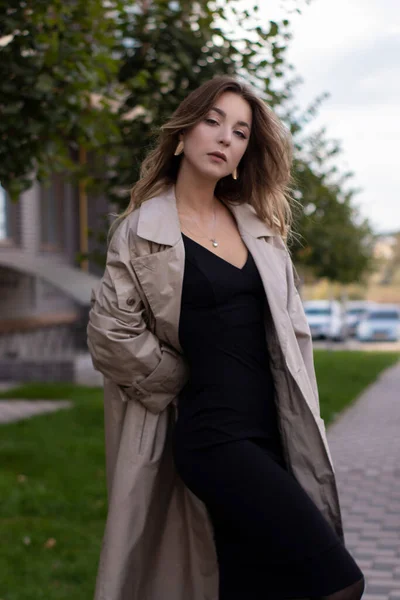 Atraktivní štíhlé mladé brunetky v módní trenč kabát a černé šaty — Stock fotografie