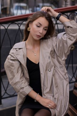 şık trençkotlu ve bankta oturan siyah elbiseli çekici, zayıf, genç bir esmer. Sonbahar, sarı yapraklar