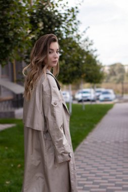 şık trençkotlu ve siyah elbiseli çekici, zayıf, genç bir esmer.