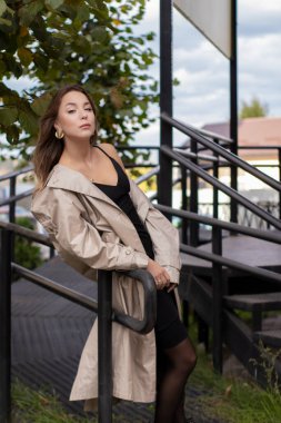 şık trençkotlu ve merdivenlerin yanında yürüyen siyah elbiseli güzel, zayıf, genç bir esmer. Sonbahar, sarı yapraklar.