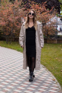 Havalı siperlerde, siyah elbiseli ve parkta güneş gözlüklü çekici, zayıf, genç bir esmer. Sonbahar, sarı yapraklar