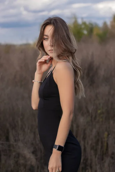 フィールド内のスキニーフィッティングブラックドレスで敏感な魅力的なスリムブルネット。秋黄色の葉青い空 — ストック写真