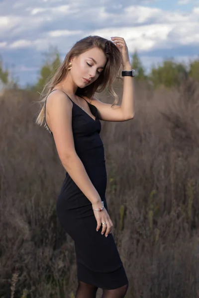 Sensible attraktive schlanke Brünette in dünn anliegendem schwarzen Kleid im Feld. Herbst, gelbe Blätter, blauer Himmel — Stockfoto