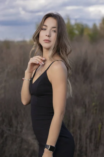 Morena magro atraente sensível em vestido preto magro encaixe no campo. outono, folhas amarelas, céu azul — Fotografia de Stock