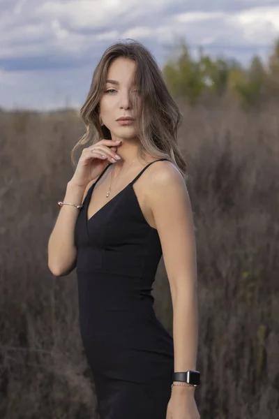 フィールド内のスキニーフィッティングブラックドレスで敏感な魅力的なスリムブルネット。秋黄色の葉青い空 — ストック写真