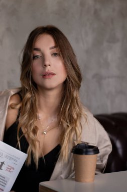 Gri çatı katındaki trençkotlu esmer, deri koltukta, kağıt bardakla. şehir yaşam tarzı kavramı