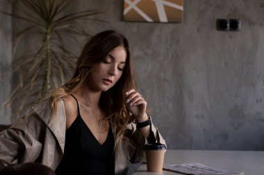 Gri çatı katındaki trençkotlu esmer, deri koltukta, kağıt bardakla. şehir yaşam tarzı kavramı