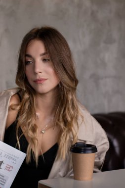 Gri çatı katındaki trençkotlu esmer, deri koltukta, kağıt bardakla. şehir yaşam tarzı kavramı