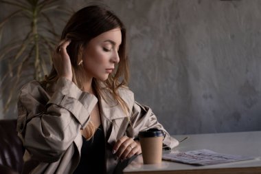 Gri çatı katındaki trençkotlu esmer, kağıt bardak ve gazeteyle deri koltukta. şehir yaşam tarzı