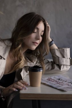 Gri çatı katındaki trençkotlu esmer, kağıt bardak ve gazeteyle deri koltukta. şehir yaşam tarzı