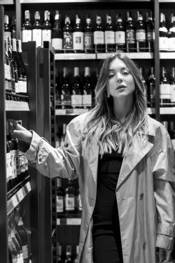 Şarapçıda rafların arasında şarap içen çekici bir kadın. siyah beyaz fotoğraf. yumuşak odak