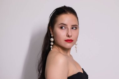 Beyaz arka planda beyaz inci küpeli siyah elbiseli çekici esmerin duygusal portresi.