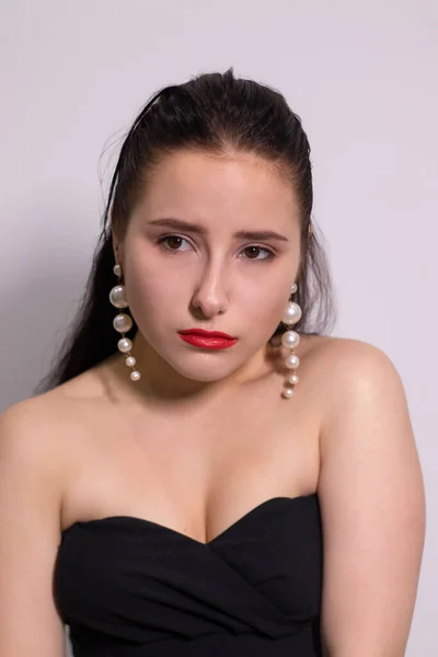 Emocjonalny portret atrakcyjnej brunetki w czarnym top z białymi perłowymi kolczykami na białym tle — Zdjęcie stockowe
