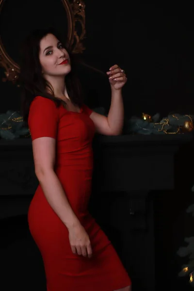 Σέξι ελκυστική μελαχρινή με κόκκινο κοκαλιάρικο φόρεμα κοντά σε χριστουγεννιάτικο δέντρο. σκοτεινή φωτογραφία. Φωτογράφηση στούντιο. συναισθηματική ηθοποιός. — Φωτογραφία Αρχείου