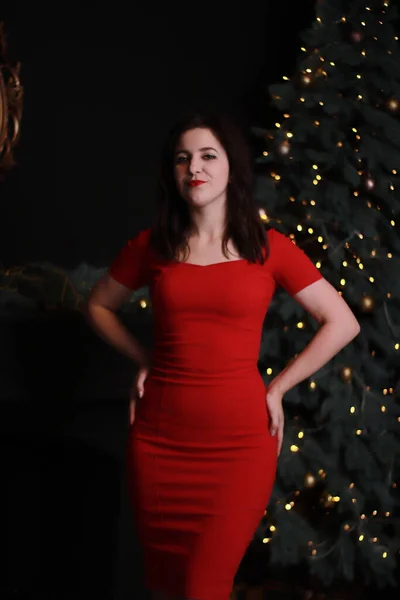 Sexy morena atractiva en vestido rojo flaco cerca de un árbol de Navidad. foto oscura. sesión de estudio. actriz emocional. —  Fotos de Stock