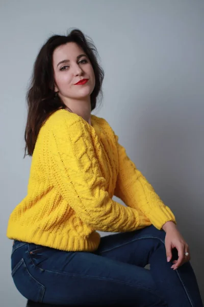 Привлекательная брюнетка в джинсах и желтом трикотажном свитере на заднем плане. студийные съемки — стоковое фото