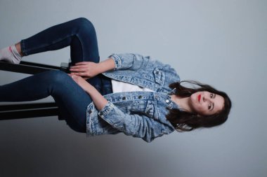 Gri arka planda kot pantolon ve kot ceketli çekici bir esmer. Stüdyo çekimi