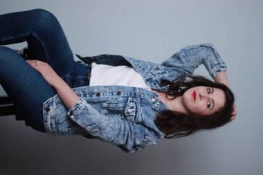 Gri arka planda kot pantolon ve kot ceketli çekici bir esmer. Stüdyo çekimi