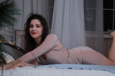 Yatağa uzanmış bej elbiseli çekici bir esmer. Stüdyo. parti, kutlama konsepti