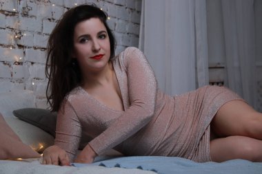 Yatağa uzanmış bej elbiseli çekici bir esmer. Stüdyo. parti, kutlama konsepti