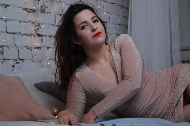 Yatağa uzanmış bej elbiseli çekici bir esmer. Stüdyo. parti, kutlama konsepti