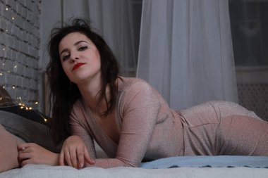 Yatağa uzanmış bej elbiseli çekici bir esmer. Stüdyo. parti, kutlama konsepti