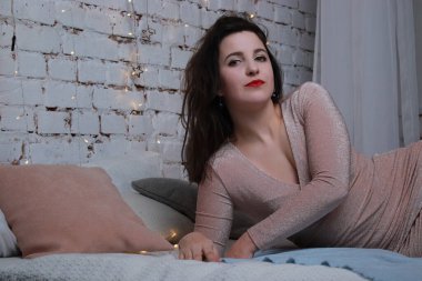 Yatağa uzanmış bej elbiseli çekici bir esmer. Stüdyo. parti, kutlama konsepti