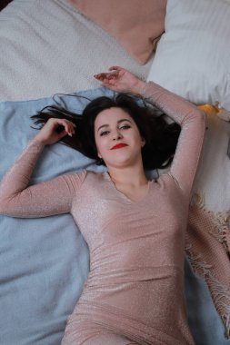 Yatağa uzanmış bej elbiseli çekici bir esmer. Stüdyo. parti, kutlama konsepti