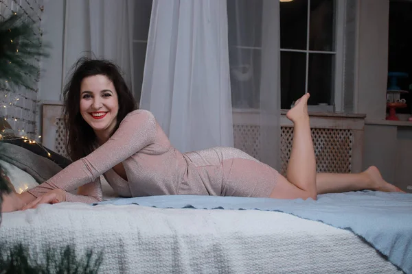 Sexy morena atractiva en vestido beige acostado en una cama. sesión de estudio. fiesta, concepto de celebración — Foto de Stock