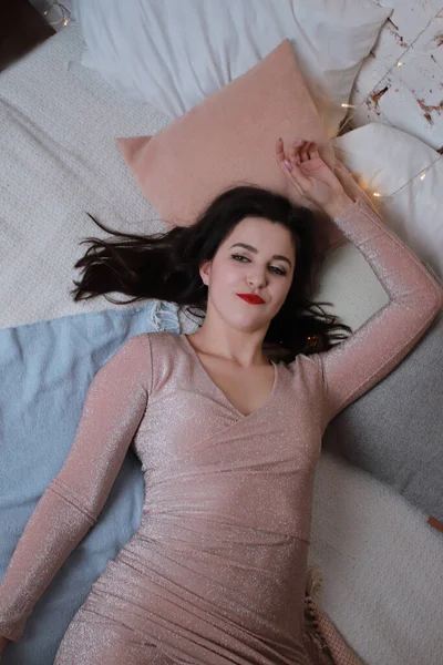 Sexy attraktive Brünette in beigem Kleid auf einem Bett liegend. Studioaufnahmen. Party, Festkonzept — Stockfoto