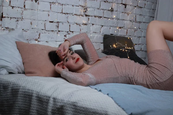 Сексуальная привлекательная брюнетка в бежевом платье лежащая на кровати. Студийные съемки вечеринка, концепция праздника — стоковое фото