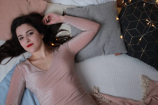 Sexy atraktivní brunetka v béžových šatech ležící na posteli. Studio natáčení. párty, koncepce oslav — Stock fotografie