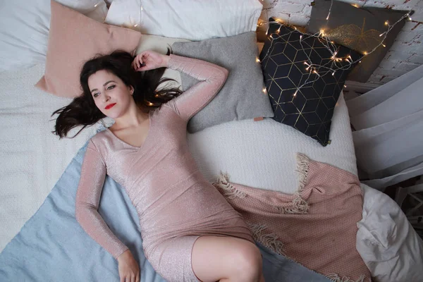 Sexy atraente morena em vestido bege deitado em uma cama. filmagens. festa, conceito de celebração — Fotografia de Stock